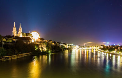 Illuminated buildings by river against sky at night