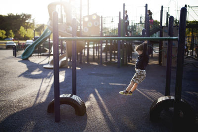 Side view full length of boy hanging from monkey bars at playground