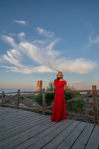 A female model posing in a red dress during sunrise along the coastline of the mediterranean