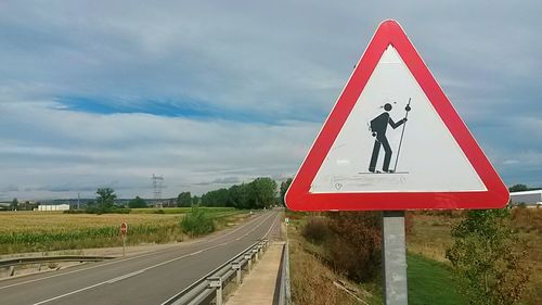 Road sign on country road against sky