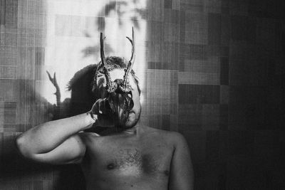 Shirtless man holding animal skull against patterned wall