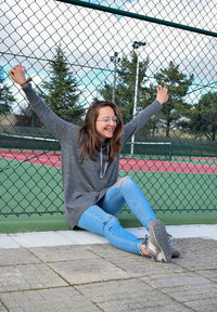 Portrait of happy young woman holding umbrella while standing on chainlink fence