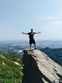 Man standing on rock with arms outstretched against sky