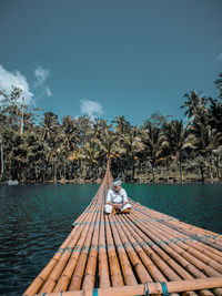 Man sitting on wooden raft over lake against trees