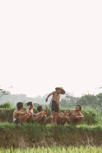 People relaxing on field against clear sky