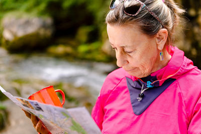 Senior female hiker watching paper map on mountain behind casano river in spain