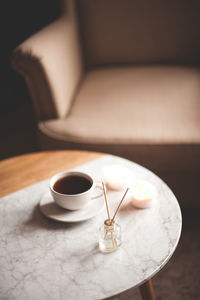 Liquid home fragrance with glass bottle and wooden sticks, cup of fresh tea staying on marble 