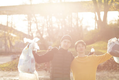 Portrait of young male volunteers with plastic garbage standing in public park