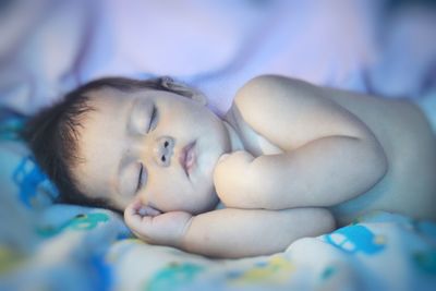 Close-up of shirtless cute baby girl sleeping on bed at home