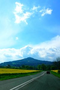Empty road leading towards mountains against sky