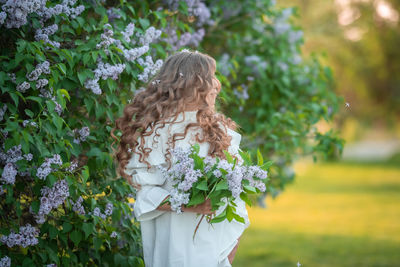 Rear view of woman standing by flowering plants