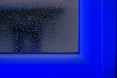Close-up of blue neon window with water drops