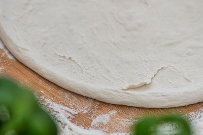 Dough for pizza on a wooden board with white flour and ingredients around ready for preparation
