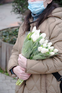 A woman in a raincoat and a mask with a bouquet of white spring tulips