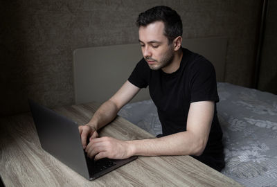 Young pensive, serious man works at home in a room with laptop 