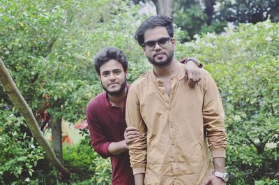 Portrait of young male friends standing against plants