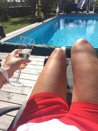 Midsection of woman having champagne while relaxing against swimming pool