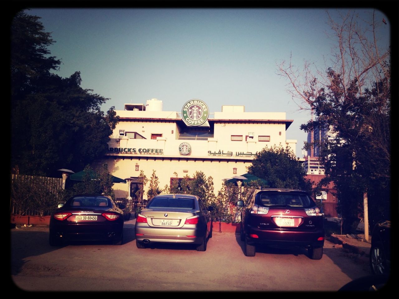 car, building exterior, land vehicle, architecture, transfer print, transportation, built structure, street, mode of transport, tree, clear sky, auto post production filter, city, road, parking, city street, residential structure, residential building, parked, incidental people