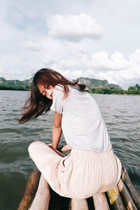 Portrait of woman sitting on wooden raft over lake against sky