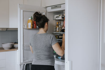 Rear view of woman standing in front of open fridge