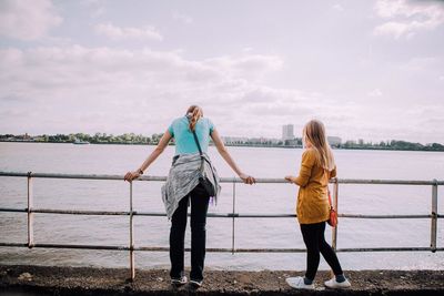 Female friends standing by river against sky