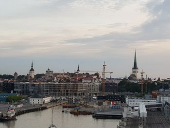 Sailboats in river by buildings in city against sky