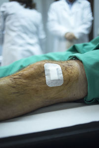 Midsection of patient knee with adhesive bandage on bed 