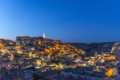 Illuminated buildings in city against clear blue sky