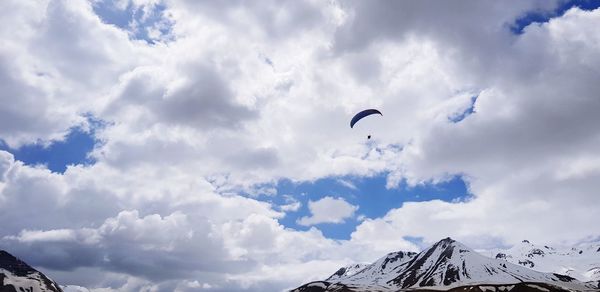 Low angle view of people flying over snowcapped mountain against sky