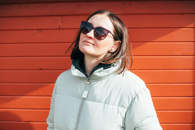 Portrait of young woman wearing sunglasses standing against brick wall