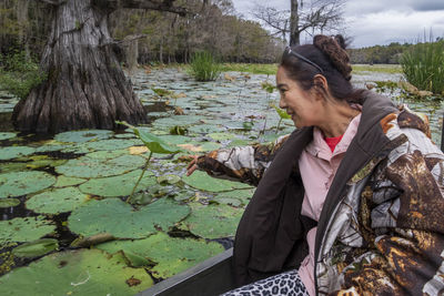 Smiling senior woman touching leaf while sitting on boat