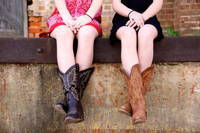 Low section of women wearing designed boots while sitting on retaining wall in city