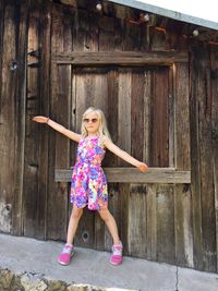 Full length of girl standing against wooden cottage