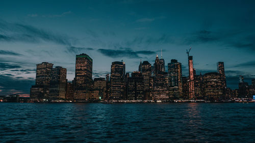 Illuminated buildings by sea against sky at dusk