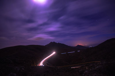 Illuminated road by mountains against sky at night