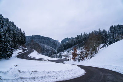 Snow covered road by trees against sky