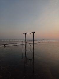 Wooden posts on beach against sky during sunset