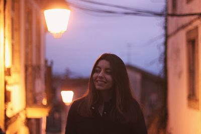 Portrait of smiling young woman against illuminated building