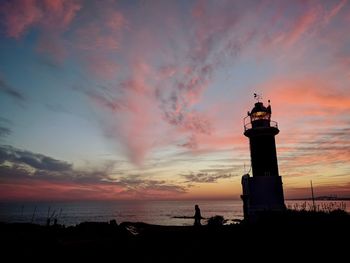 Silhouette lighthouse by sea against sky during sunset