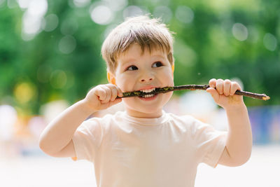 Little caucasian boy plays outdoors in the park with a stick from a tree, bites it