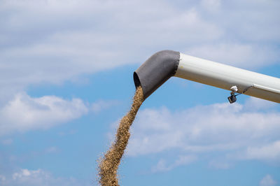 Crops falling from combine harvester against sky