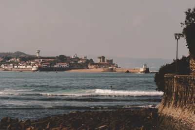 Scenic view of sea against buildings in city against clear sky