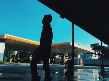 Silhouette man standing on street against blue sky