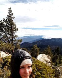 Portrait of young woman against tree mountains against sky