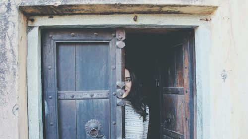 Portrait of smiling beautiful woman standing behind door