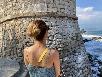 Rear view of woman standing against stone wall