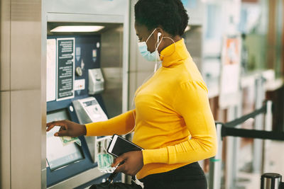 Dubai, uae, november 2020 african woman wearing a protective mask withdraws money from a bank card 