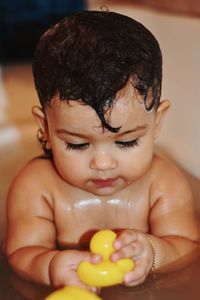 Close-up of cute baby girl playing with rubber duck while bathing in bathtub