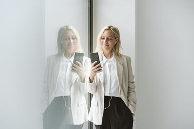 Businesswoman looking at mobile phone at glass wall