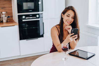 Woman using phone while sitting on table at home